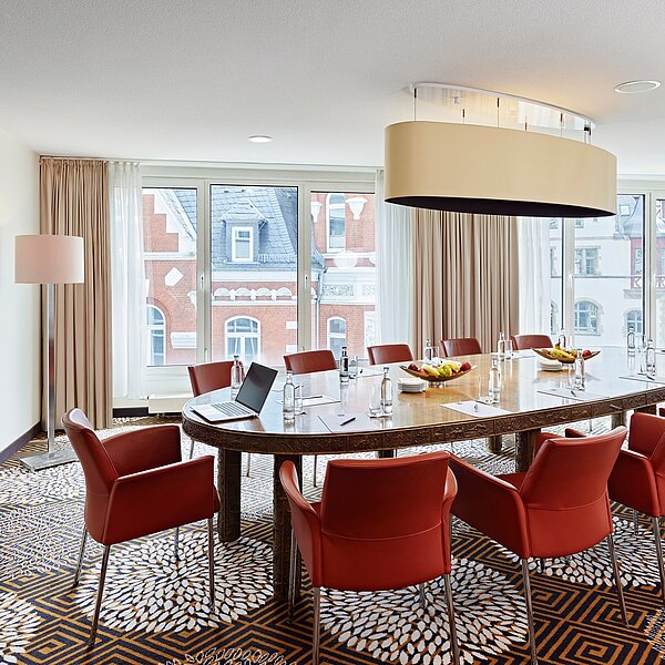 Stilvoller Boardroom mit gemustertem Teppichboden, dunklem Besprechungstisch mit roten Stühlen und Fenster mit Ausblick auf die Fassade eines schicken Altbaus