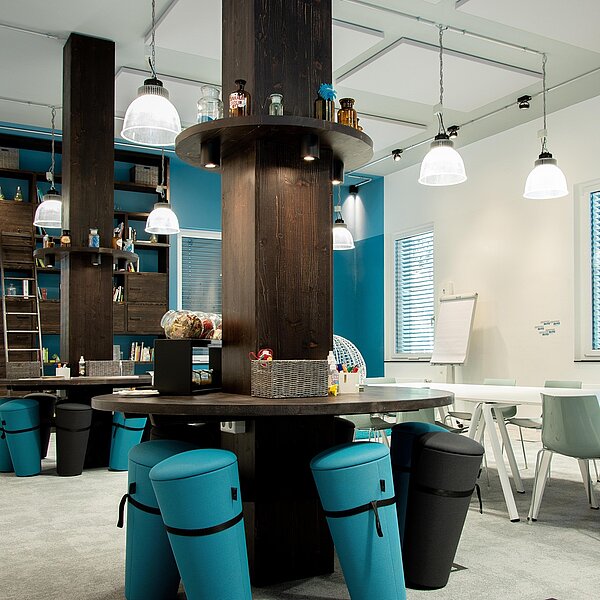 Kreativraum mit türkis-schwarzen Sitzgelegenheiten, dunklen Holzelementen und auffälligen Hängeleuchten