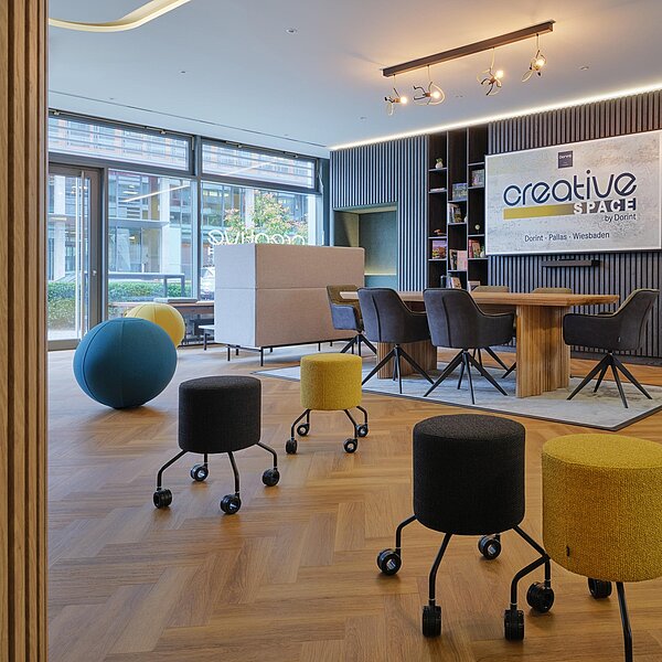 Heller Besprechungsraum mit großer Fensterfront, bunten Sitzgelegenheiten und Holzboden