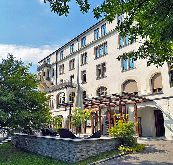 Das Bild zeigt die ruhige und einladende Außenansicht eines Hotels mit einem modernen Anbau an einem sonnigen Tag.