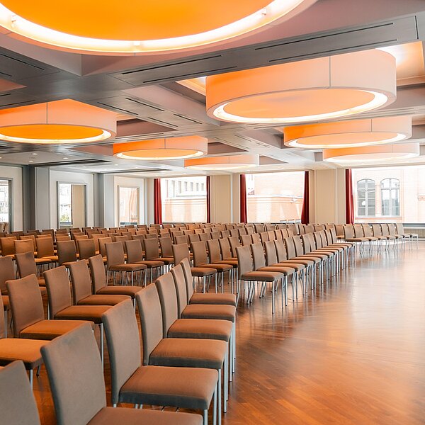 Eventraum mit braunen Stuhlreihen und auffälligen großen orangenen Deckenleuchten