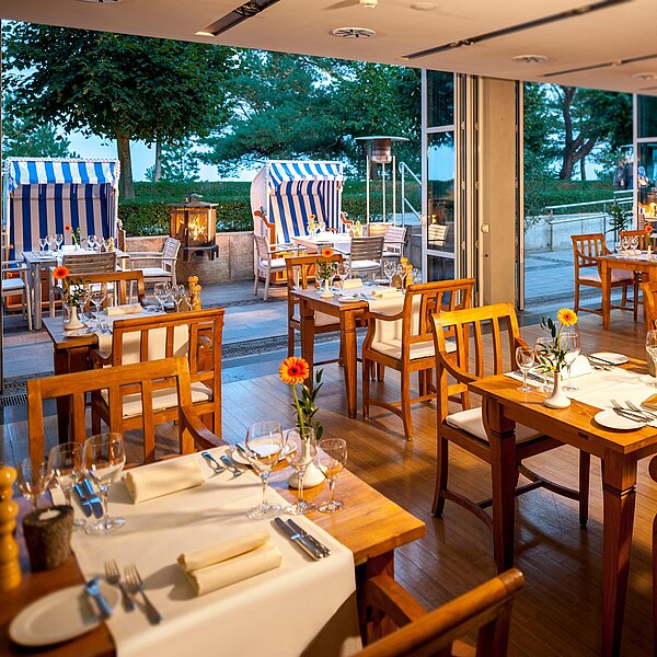 Gedeckte Tisch in einem Strandlokal mit geöffneten Terrassentüren und Strandkörben auf der Terrasse