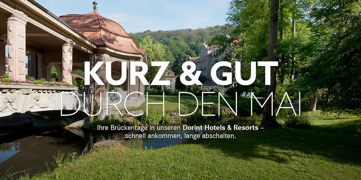 Schriftzug Kurz & Gut durch den Mai im Vordergrund, im Hintergrund Pavillon, grüne Wiese und Wasser
