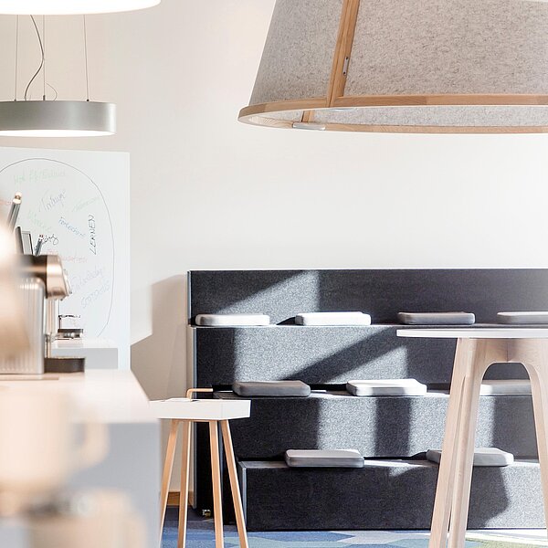 Heller Kreativraum mit grauer Sitztribüne, Kaffeemaschine und Besprechungsinseln