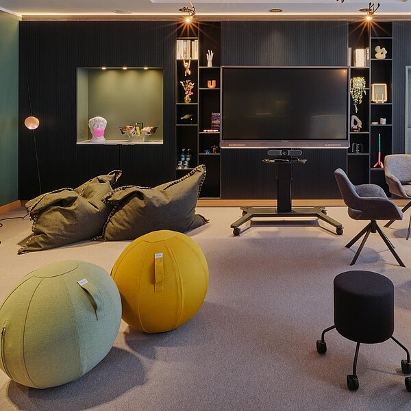 Meetingraum mit bunten Sitzgelegenheiten, inspirativer Deko und Monitor