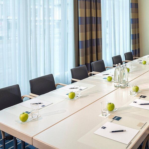 Besprechungsraum mit Tischblock und gemusterten Vorhängen im Hintergrund