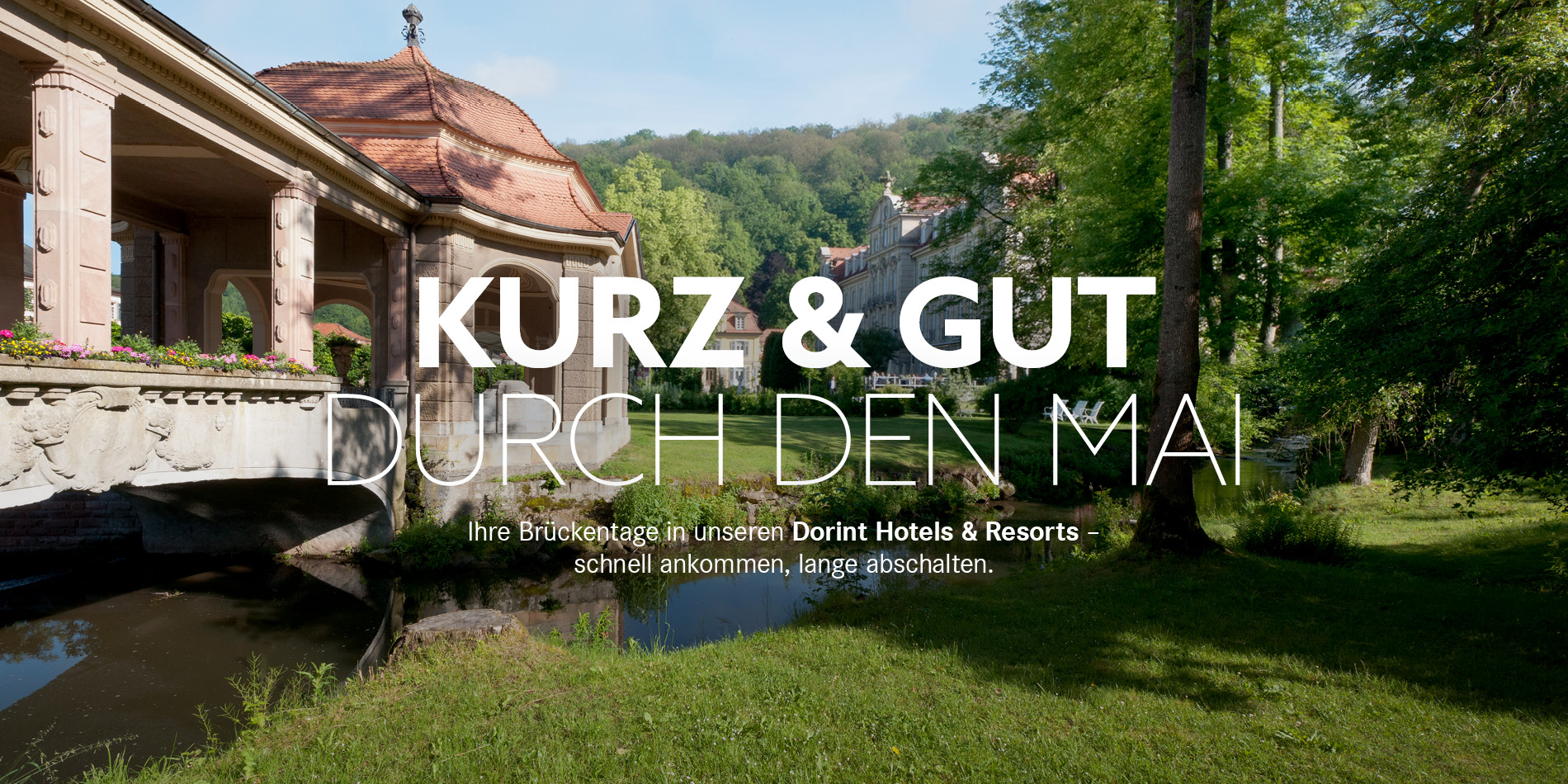 Schriftzug Kurz & Gut durch den Mai im Vordergrund, im Hintergrund Pavillon, grüne Wiese und Wasser