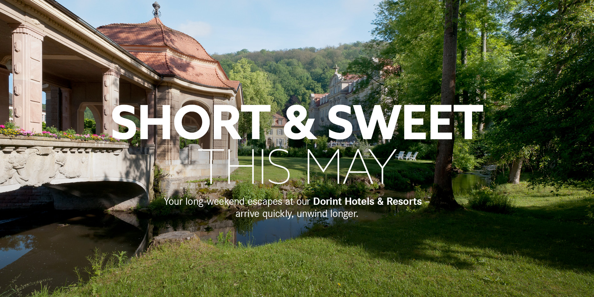 The words “Short & Sweet this May” in the foreground, with a pavilion, a green meadow, and water in the background