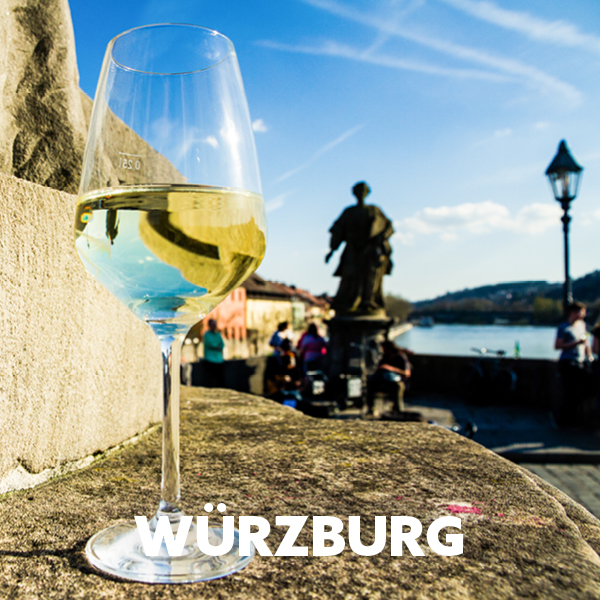 Ein Weinglas mit Weißwein steht im Vordergrund, mit der Stadt Würzburg im Hintergrund.