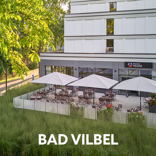 Das Bild zeigt die Außenterrasse des Restaurants "Brasserie Moulins" in Bad Vilbel, die mit mehreren Sonnenschirmen ausgestattet ist und mit Tischen und Stühlen für Gäste bestückt ist.