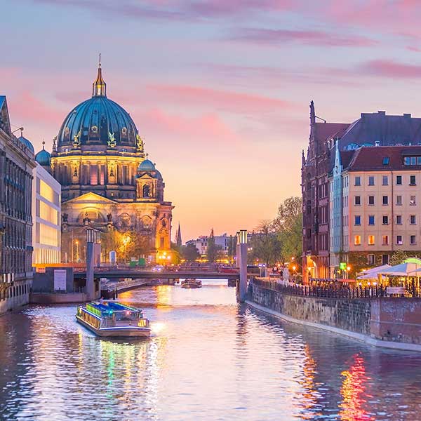 Das Bild zeigt einen romantischen Blick auf den Berliner Dom bei Sonnenuntergang, mit einem Ausflugsboot auf der Spree.